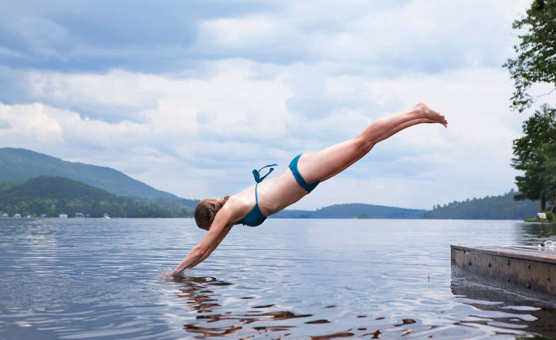 Mädchen springt mit einem Kopfsprung vom Badesteg in den See.